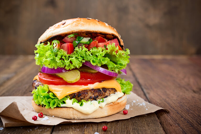 Un gros burger rempli d’ingrédients comme des tomates, de la salade, des oignons et de la salsa pour ajouter du piquant.