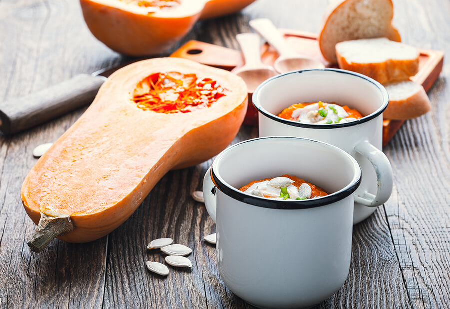 Recette de potage à la courge Butternut dans une tasse avec une courge Butternut coupée en deux à côté
